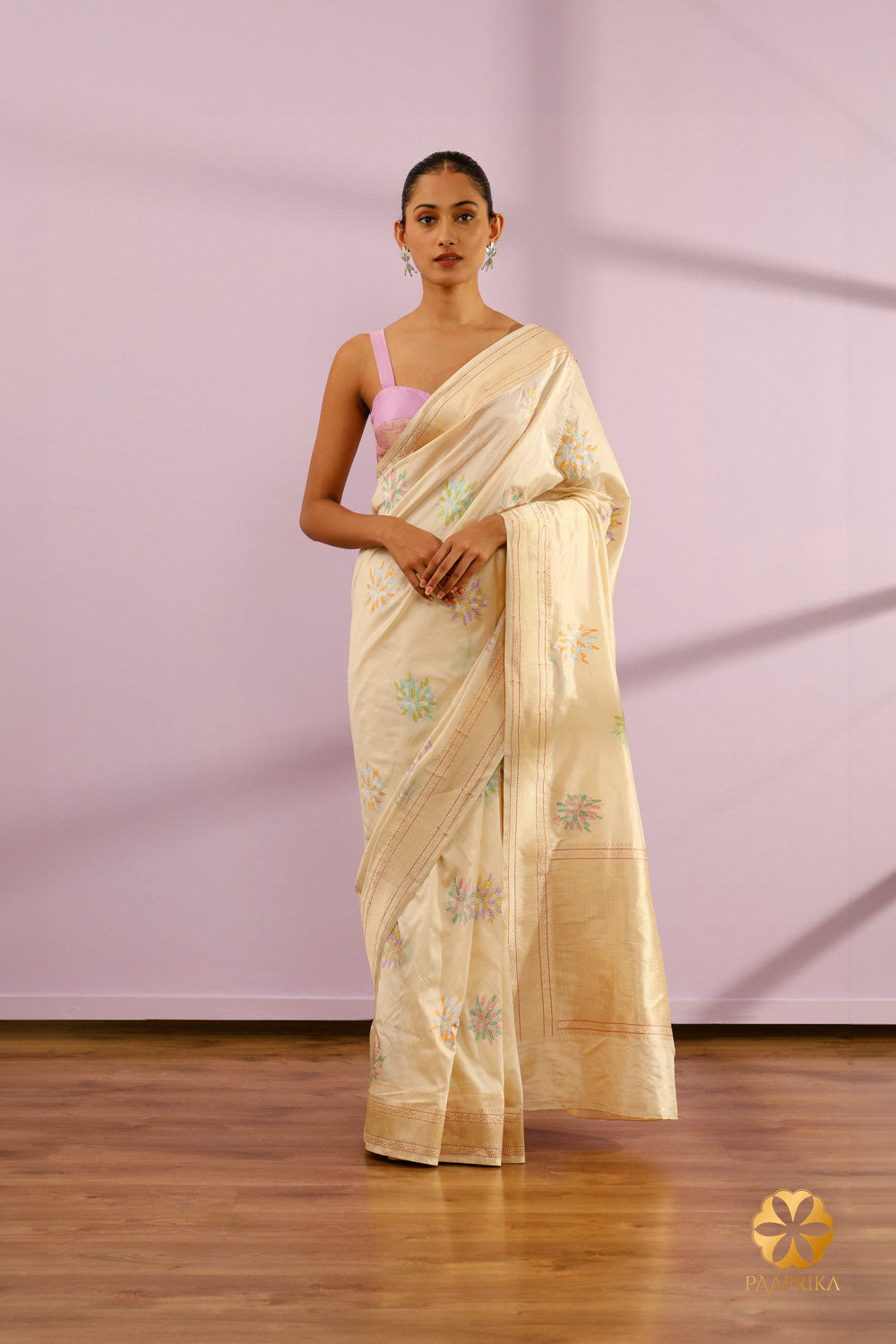 A full view of the "Elegant Ivory Banarasi Saree." The ivory saree is elegantly draped, showcasing its pristine color and the intricate pastel floral motifs running along its length.