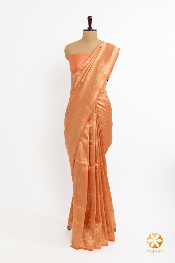 A Pastel Peach Banarasi Brocade Saree paired with a soft gold blouse featuring intricate embroidery.