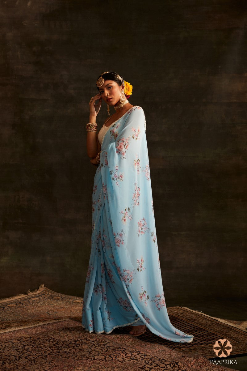 A stylish woman confidently wearing the Gorgeous Aqua Blue Floral Printed Georgette Saree, making a fashion statement with poise. The saree's floral prints enhance her ensemble, exuding charm and sophistication.