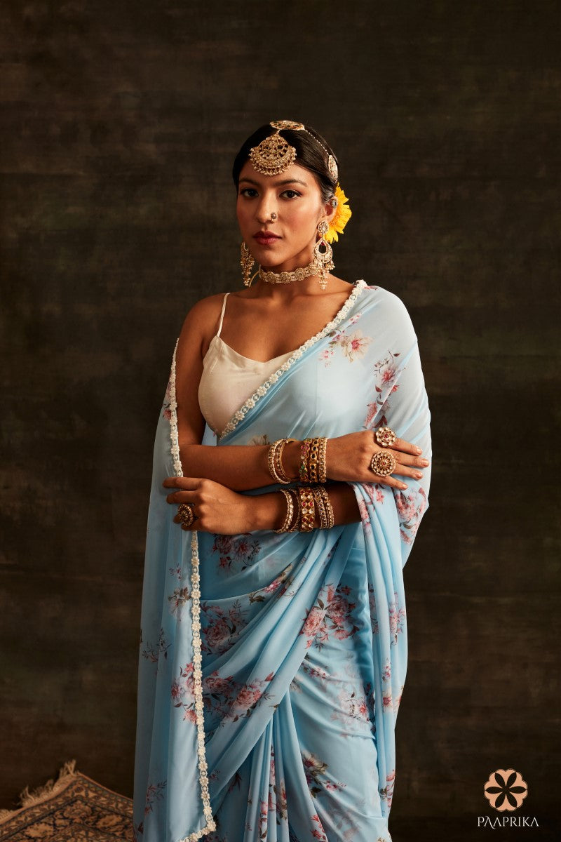 Gorgeous Aqua Blue Floral Printed Georgette Saree paired with complementary accessories. The saree's aqua blue hue and delightful floral prints create a captivating look, perfectly complemented by the accessories for a stylish and harmonious appearance.